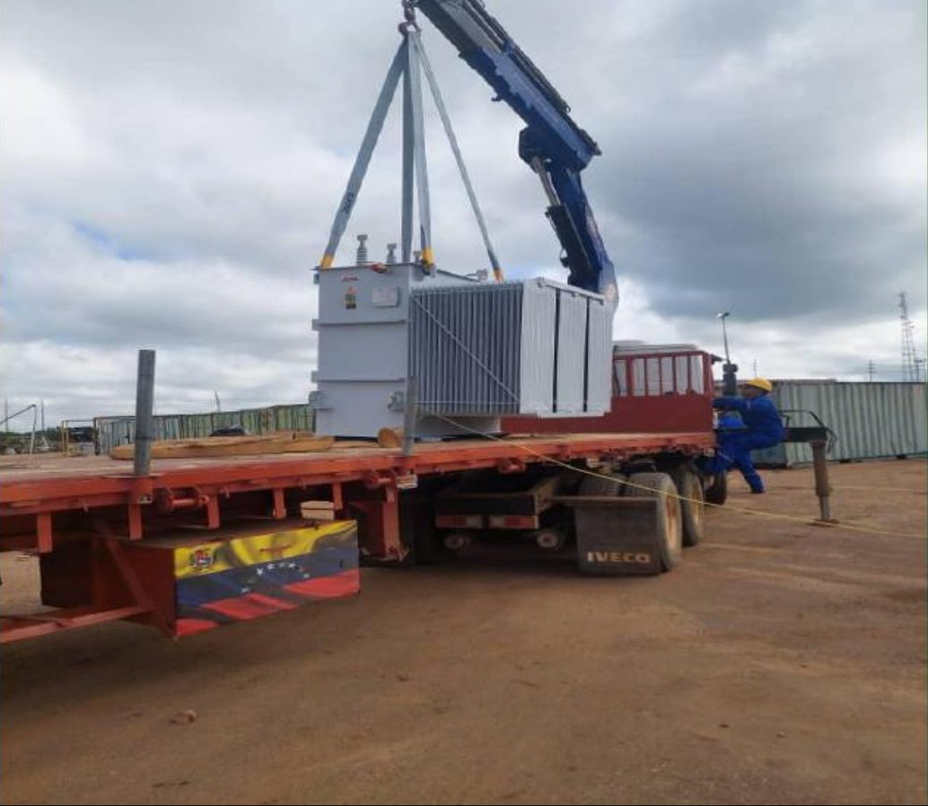 Hydraulic boom lifting industrial equipment over a flatbed truck